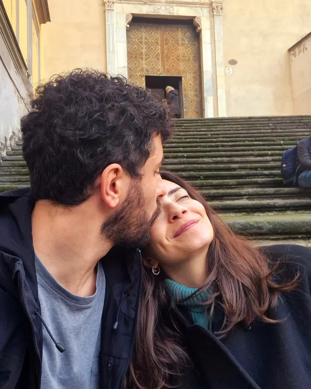 Ottavia e Filippo seduti su una scalinata: lui le dà un bacio sulla fronte, lei sorride con gli occhi chiusi.